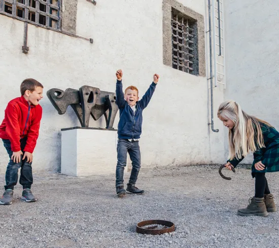 Kinder spielen Ringwurf im Innenhof neben abstrakter Metallskulptur
